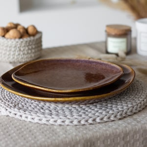 May include: Two brown ceramic plates stacked on a white crocheted placemat on a beige tablecloth.