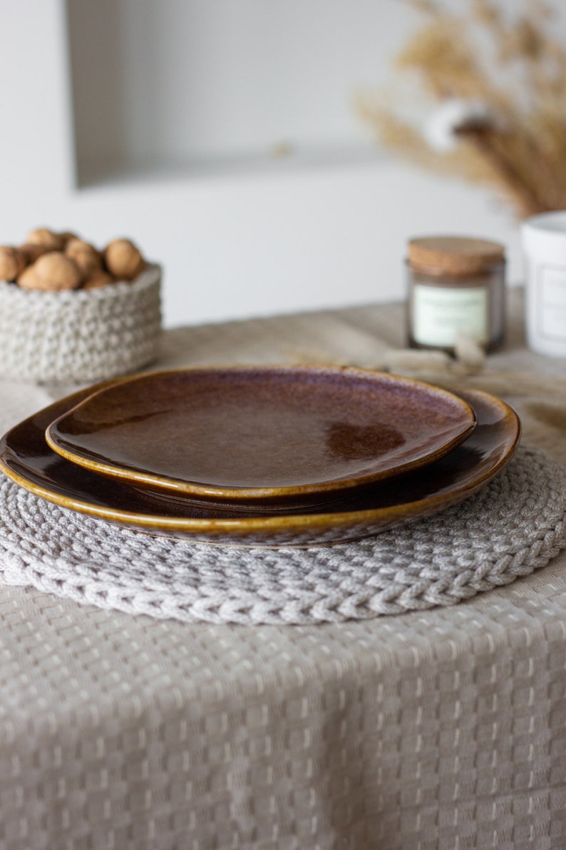 May include: Two brown ceramic plates stacked on a white crocheted placemat on a beige tablecloth.