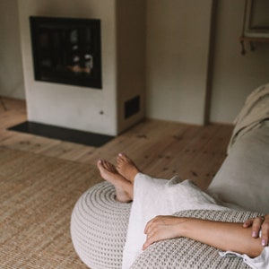 K&ouml;nnte beinhalten: Eine Person entspannt sich auf einem wei&szlig;en Sofa mit einem gestrickten Fu&szlig;hocker und einem Kissen. Das Sofa steht in einem Raum mit einem Kamin und Holzboden.