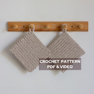 Puede incluir: Dos agarraderas de olla de crochet beige colgadas en un estante de madera con el texto "CROCHET PATTERN PDF & VIDEO"