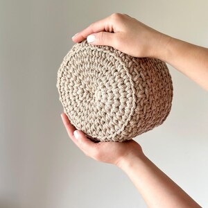 May include: A beige crocheted round basket, held in two hands.