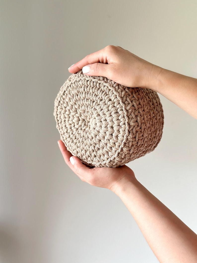 May include: A beige crocheted round basket, held in two hands.