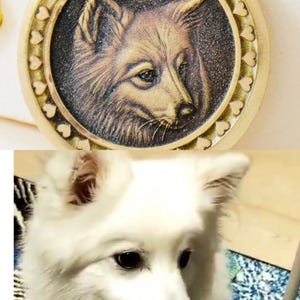 May include: A gold-colored pendant with a detailed relief of a dog's face, surrounded by a border of small hearts. The word "YOGHURT" is inscribed at the top. The image also shows a white dog.
