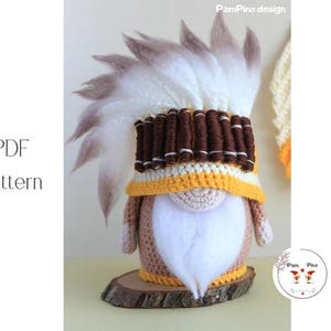 May include: A handmade gnome doll with a Native American headdress. The gnome has a white beard, a yellow and brown hat, and a brown body. The headdress is made of white and brown feathers. The doll is on a wooden base. The text "PDF Pattern" is visible.