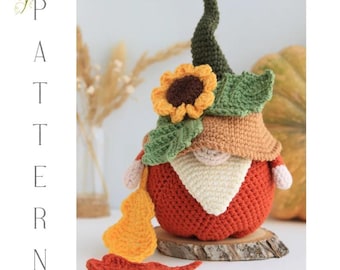 May include: A handmade crochet gnome with a red body, tan hat, and green leafy accents. A yellow sunflower and a long green hat top the gnome. The gnome has a white beard and a small nose. The gnome is decorated with a yellow gourd and a red leaf.