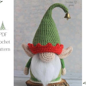May include: A crocheted Christmas elf gnome with a green hat, red crown, and white beard. The gnome has beige ears and a small gold bell on the hat. The image also includes the text "PDF Crochet Pattern".