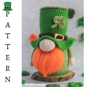 May include: A handmade crochet gnome in green, orange, and beige, with a long orange beard and a green hat. The gnome is on a wooden base, with a shamrock and the word "PATTERN" in the image.