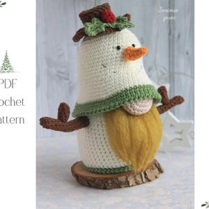 May include: A handmade crochet snowman gnome with a white body, orange nose, and a yellow beard. It has a brown hat with green leaves and a red berry. The gnome is on a wooden base. The text "Snowman gnome" is visible.