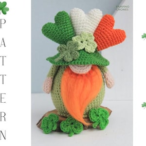 Könnte beinhalten: Ein handgefertigter Häkelzwerg mit grünem Körper, grünem Hut und orangefarbenem Bart. Der Zwerg hat ein Kleeblatt auf seinem Hut und drei herzförmige Akzente in Grün, Weiß und Orange. Das Wort "PATTERN" steht vertikal links.