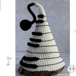 May include: A white crocheted musical tree with black piano keys and a black treble clef. The tree is set on a wooden base. The word "PATTERN" is written vertically on the left side of the image.