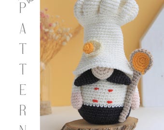 May include: A handmade crochet chef gnome wearing a white chef's hat and uniform, holding a wooden spoon. The gnome has a black mustache and is standing on a wooden slice. The image includes the text "PATTERN" and "PAMPINO GNOMES".
