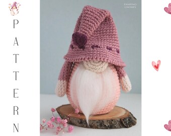 Könnte beinhalten: Ein handgehäkelter Zwerg mit rosa Hut und Körper, weißem Bart und beigen Armen. Der Zwerg sitzt auf einer Holzscheibe. Das Wort "PATTERN" wird vertikal auf der linken Seite des Bildes angezeigt. Das Bild enthält auch den Text "PAMPINO GNOMES".