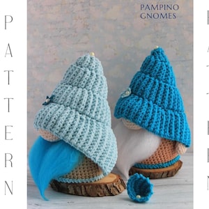 May include: Two handmade gnome figures with blue and light blue crocheted hats and beards. The gnomes are on wooden bases. The image includes the text "PAMPINO GNOMES PATTERN".