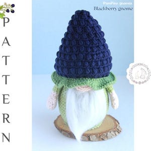 May include: A handmade crochet gnome with a dark blue textured hat, green collar, and a long white beard. The gnome is set on a wooden slice. The text "Blackberry gnome" is visible.