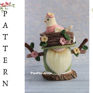 May include: A crochet gnome with a bird in a nest design. The gnome features a white beard, a green body, and a brown hat with a bird on top. The design includes floral accents and is set on a wooden base. The word "PATTERN" is written vertically on the left.