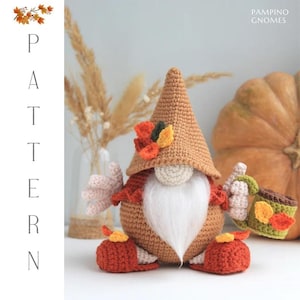 May include: A crocheted gnome doll with a brown pointed hat, white beard, and holding a small mug. The gnome is wearing a red and brown outfit with orange and yellow leaf accents. The word "PATTERN" is vertically displayed on the left.