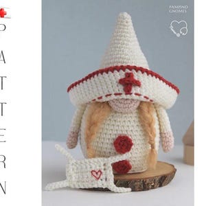 May include: A handmade crochet nurse gnome with a white hat and red cross emblem. The gnome has blonde braids, a red heart on its belly, and a matching mask with a heart. The gnome is displayed on a wooden slice.