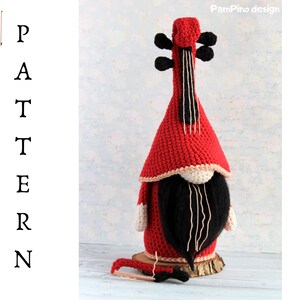 May include: A handmade red and black crochet gnome shaped like a violin. The gnome has a long black beard, a red hat, and a white trim. The text "PATTERN" is on the left side of the image.