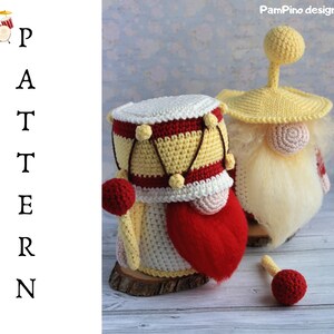 May include: Crocheted drum and gnome pattern. The drum is yellow, red, and white, with a red mallet. The gnome has a yellow hat and a long white beard. The word "PATTERN" is written vertically on the left.