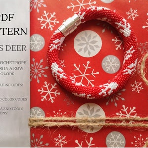 May include: A red and white beaded crochet rope bracelet with a reindeer design. The bracelet is on red and white snowflake patterned wrapping paper. The text "PDF PATTERN XMAS DEER" is visible in the top left corner of the image. The text "BEAD CROCHET ROPE 17 BEADS IN A ROW 2 COLORS" is visible below the title. The text "PDF FILE INCLUDES: CHARTS PHOTOS SEED BEAD COLOR CODES TIPS MATERIALS AND TOOLS SUGGESTIONS" is visible in the bottom left corner of the image.