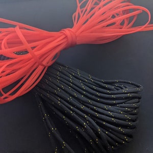 Könnte beinhalten: Nahaufnahme von zwei Garnrollen, eine rot und eine schwarz mit gelben Akzenten. Ein goldfarbener Stecker ist ebenfalls sichtbar.