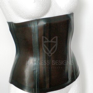 May include: A black latex corset with a shiny finish and a single seam down the front. The corset has a  "Harness Designs" logo on the front.
