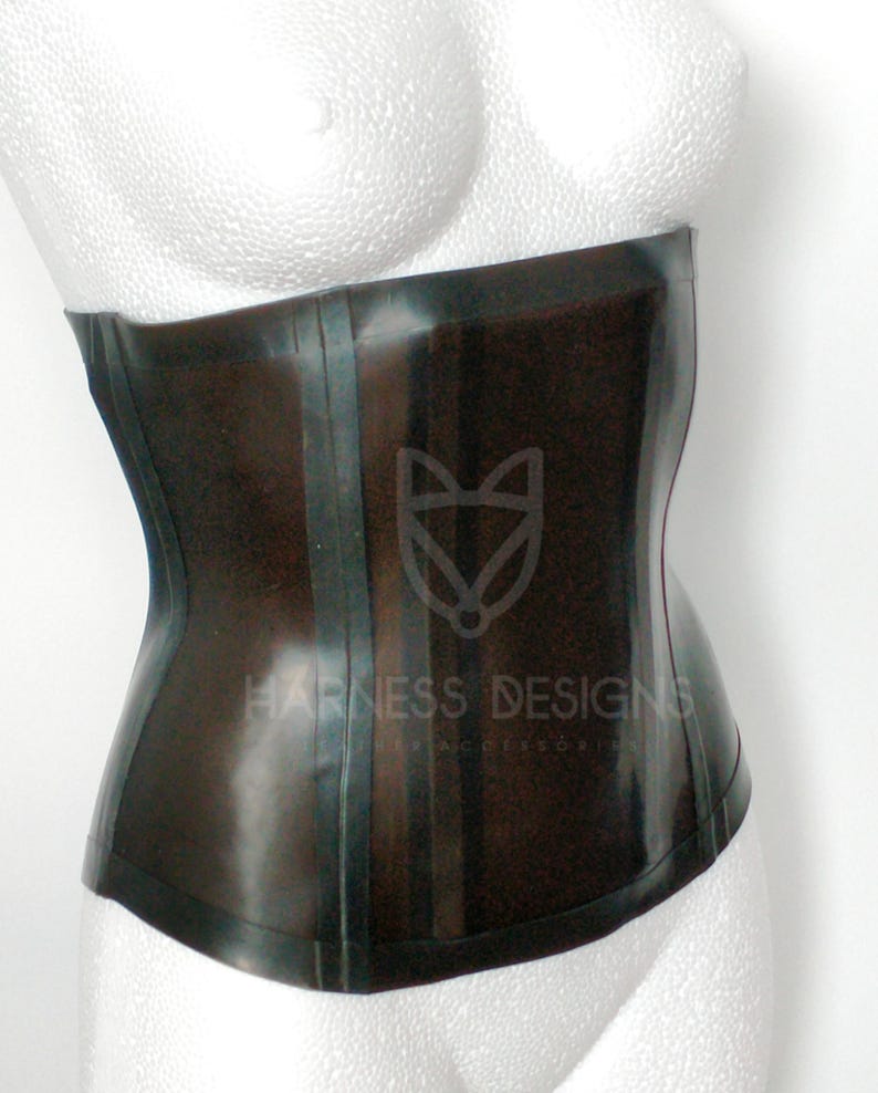 May include: A black latex corset with a shiny finish and a single seam down the front. The corset has a  "Harness Designs" logo on the front.