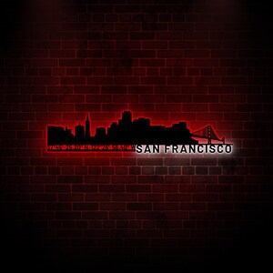 May include: A neon sign depicting the San Francisco skyline with the Golden Gate Bridge, coordinates, and the text "SAN FRANCISCO". The sign is against a red brick wall background.