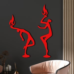 May include: Two red silhouette wall sculptures of people with flames on their heads. The figures are in a dancing pose.