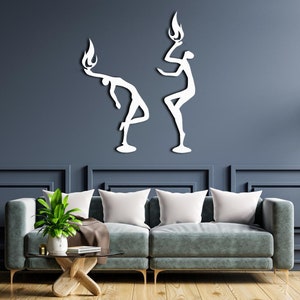 May include: Two white metal wall sculptures of stylized figures with flames on their heads. The figures are posed in a dynamic, abstract style. The sculptures are mounted on a dark blue wall.