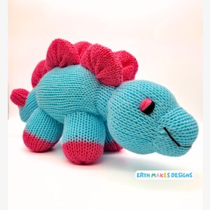 Light blue knitted Stegosaurus with pink spikes and feet. With the logo, Eryn Makes Designs.