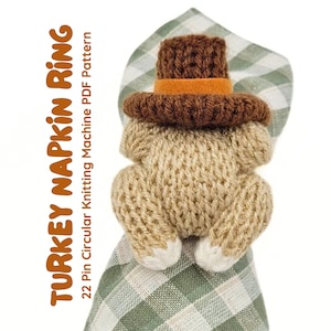 May include: A knitted turkey napkin ring with a brown pilgrim hat and an orange band. The turkey is beige with white accents and is holding a green and white checkered napkin. Text on the left says "TURKEY NAPKIN RING".