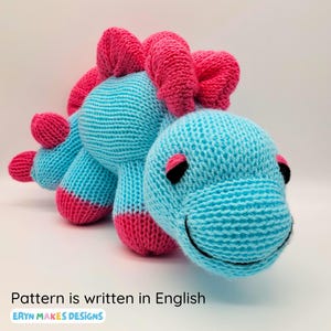 Light blue knitted Stegosaurus with pink spikes and feet. With the logo, Eryn Makes Designs, and the subtitle, Pattern is written in English.