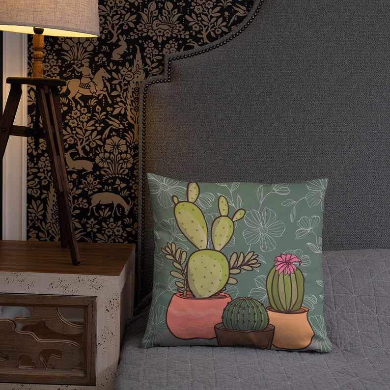 Puede incluir: Una almohada verde con un patr&oacute;n floral y un dise&ntilde;o de tres cactus en maceta. Los cactus son verdes, amarillos y rosas. Las macetas son naranja, rosa y marr&oacute;n.