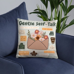 Puede incluir: Una almohada blanca con un dise&ntilde;o de sobre marr&oacute;n y flores de colores. La almohada tiene el texto "Gentle Self-Talk" y afirmaciones positivas como "Soy valioso", "Soy suficiente" y "Cada d&iacute;a es un nuevo comienzo".