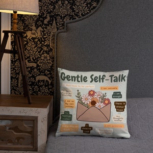 Puede incluir: Una almohada blanca con un dise&ntilde;o colorido que presenta un sobre con flores y el texto "Gentle Self-Talk" con afirmaciones positivas como "Soy valioso", "Soy suficiente" y "Cada d&iacute;a es un nuevo comienzo".