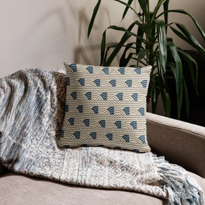 May include: A throw pillow with a cream background and a blue geometric pattern of waves and arches. The pillow is on a couch with a blue and cream throw blanket.