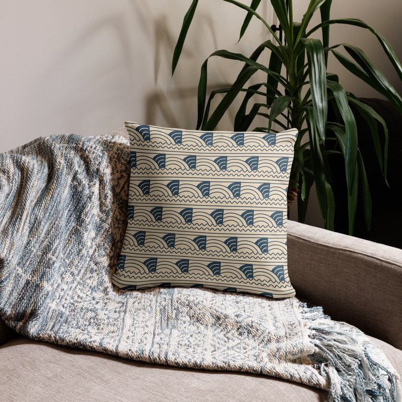 May include: A throw pillow with a cream background and a blue geometric pattern of waves and arches. The pillow is on a couch with a blue and cream throw blanket.