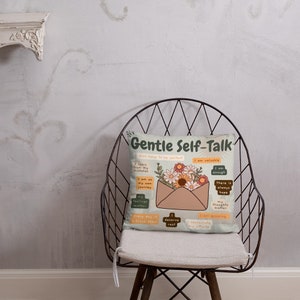 Puede incluir: Una almohada beige con un dise&ntilde;o floral y el texto "Gentle Self-Talk" en una fuente verde y marr&oacute;n. La almohada presenta un sobre marr&oacute;n con un borde blanco y un dise&ntilde;o floral. El sobre tiene varios cuadrados peque&ntilde;os con afirmaciones positivas escritas en texto negro.