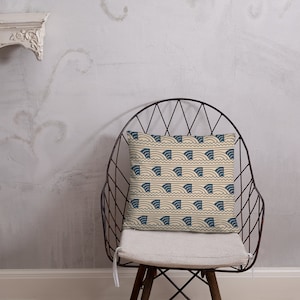 May include: A beige throw pillow with a blue and white geometric pattern of waves. The pillow is sitting on a metal chair with a white cushion.