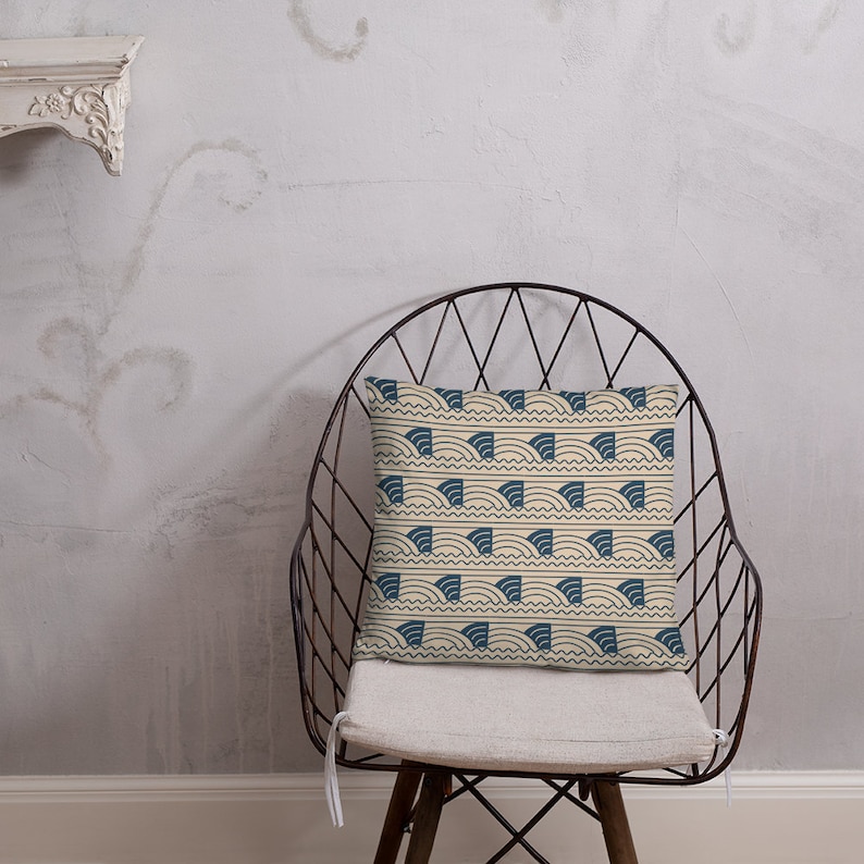 May include: A beige throw pillow with a blue and white geometric pattern of waves. The pillow is sitting on a metal chair with a white cushion.