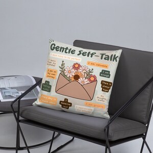 Puede incluir: Una almohada beige con un dise&ntilde;o floral y el texto "Gentle Self-Talk" con afirmaciones positivas. La almohada presenta un sobre marr&oacute;n con un dise&ntilde;o floral.