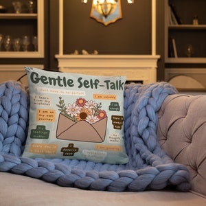 Puede incluir: Una almohada azul claro con un dise&ntilde;o floral y el texto "Gentle Self-Talk" con afirmaciones positivas. La almohada presenta un sobre estilizado con flores y el texto "No tengo que ser perfecto", "Soy valioso", "Soy suficiente", "Aprendo de mis errores", "Estoy en mi propio camino", "Mis sentimientos importan", "Cada d&iacute;a es un nuevo comienzo", "Merezco descansar", "Aprecio mis esfuerzos", "Siempre hay esperanza", "Mis pensamientos importan", "Estoy creciendo".