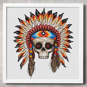 Peut inclure: Un motif de point de croix représentant un crâne portant une coiffe amérindienne colorée. Le crâne a des yeux rouges et la coiffe est ornée de plumes aux nuances de rouge, orange, jaune et marron.