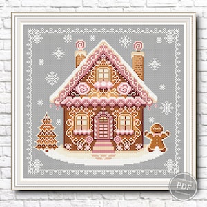 May include: A cross-stitch pattern of a gingerbread house with pink frosting, candy canes, and a gingerbread man standing in front of it. The house is surrounded by a white border and snowflakes.