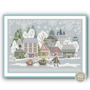 May include: A cross-stitch pattern featuring a winter village scene with houses, trees, and a person pulling a sled full of gifts. The pattern is on a blue background with white snowflakes.