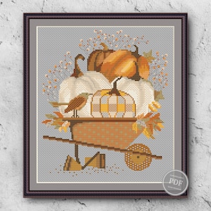 May include: Cross stitch pattern featuring a wheelbarrow filled with pumpkins, gourds, and autumn leaves. A small bird sits on the edge of the wheelbarrow. The pattern is in shades of orange, brown, and yellow.