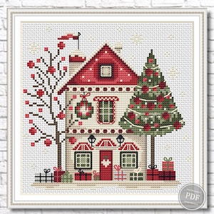 Puede incluir: Un patrón de punto de cruz que representa una casa roja y blanca con una corona de Navidad verde en la puerta, un árbol de Navidad verde con bolas rojas y un árbol rojo y blanco con bolas rojas. La casa tiene un techo rojo y molduras blancas. Hay regalos delante de la casa.