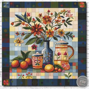 Op de afbeelding: Kruissteekpatroon met een stilleven met een vaas met bloemen, een kan en sinaasappels. De bloemen zijn oranje en geel, en de kan is versierd met bloemmotieven. De achtergrond is een patchwork van blauwe, gele en groene vierkanten.