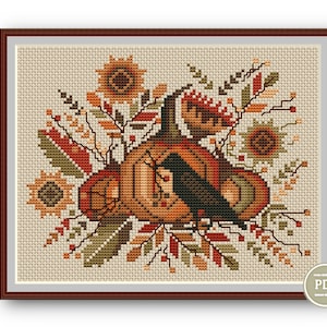 May include: Cross stitch pattern featuring a black crow perched on a pumpkin with autumn leaves and sunflowers. The pattern is in a brown frame with a "PDF" label in the corner.